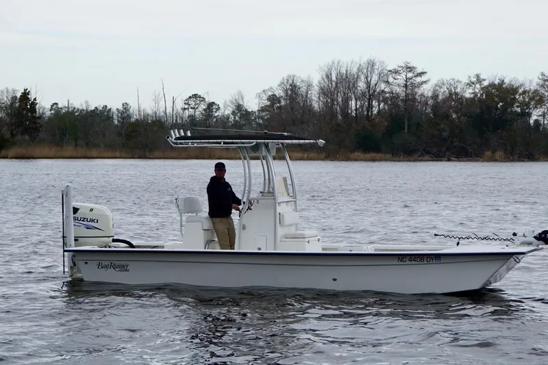 Slide: The Image of 2014 Riddick Bay Runner 2290 boat on a calm river with trees in the background. - 3
