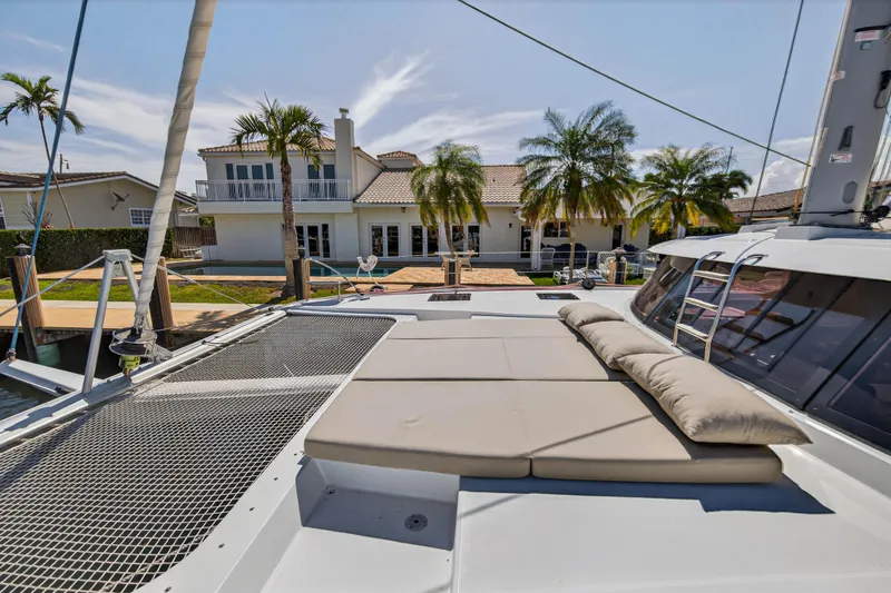 Slide: The Image of 2022 Fountaine Pajot Tanna 47 catamaran with sunbathing area, docked near a luxurious waterfront home. - 55