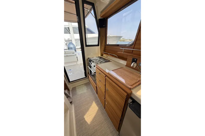 Slide: The Image of Interior of 2026 Ranger Tugs R-27, featuring a compact kitchen with wooden cabinetry. - 14