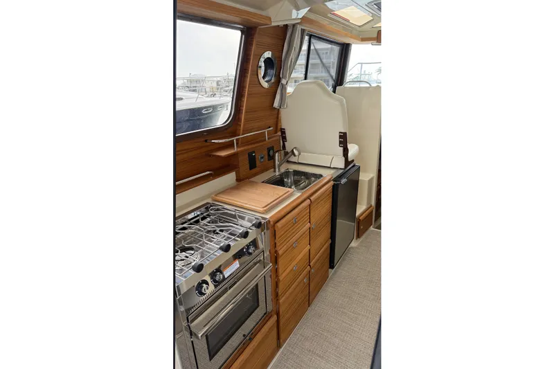Slide: The Image of Interior of 2026 Ranger Tugs R-27, featuring a compact kitchen with stove and sink. - 21