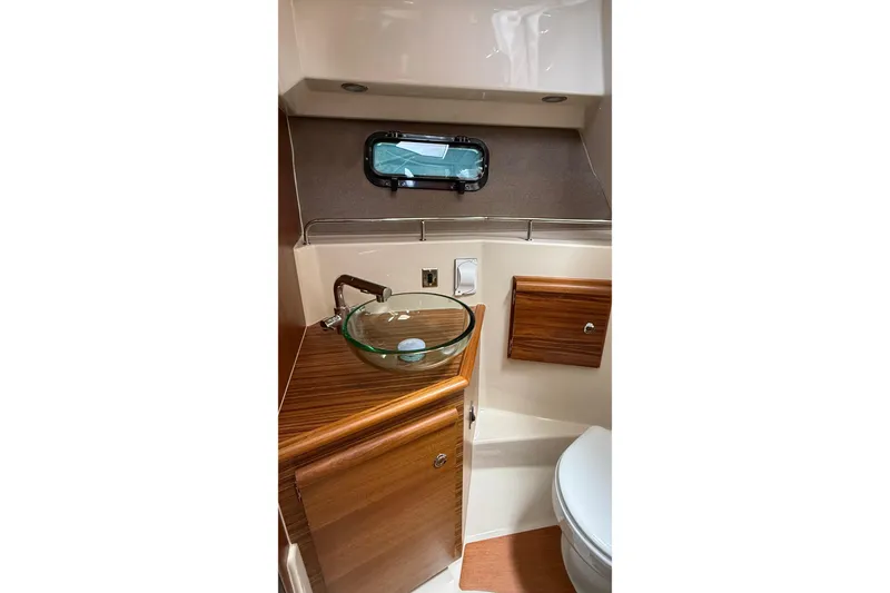 Slide: The Image of 2026 Ranger Tugs R-27 boat bathroom with glass sink and wooden cabinetry. - 29