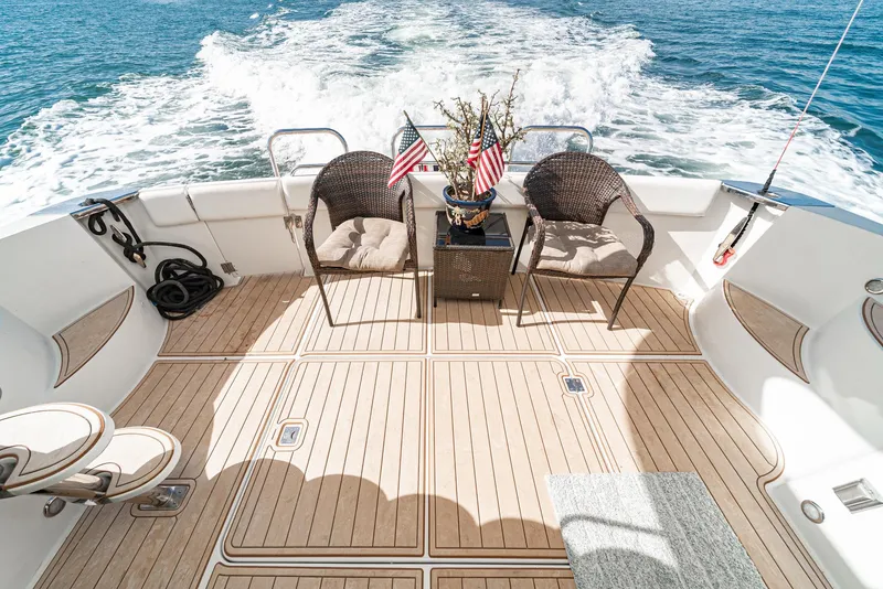 Slide: The Image of 2003 Carver 570 Voyager Pilothouse deck with chairs, table, and American flags on open water. - 25