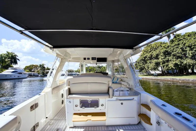 Slide: The Image of 2019 Boston Whaler 350 Realm boat interior with canopy, docked near lush greenery. - 25