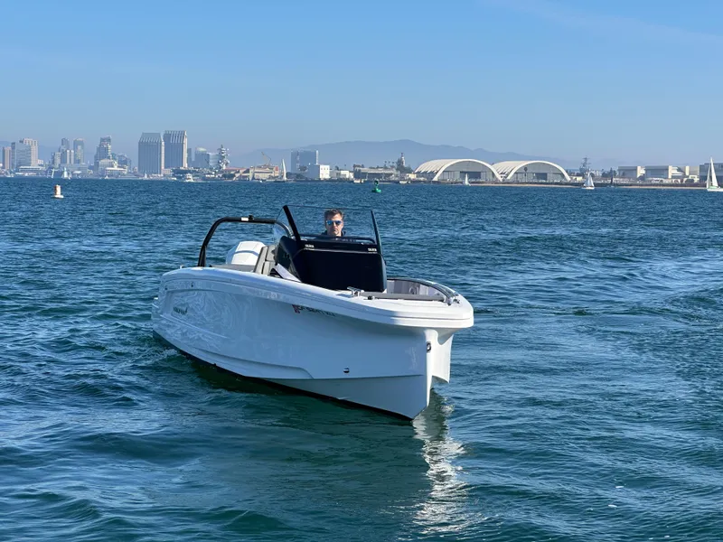 Slide: The Image of 2021 Axopar 22 Spyder cruising in a scenic harbor with city skyline backdrop. - 1