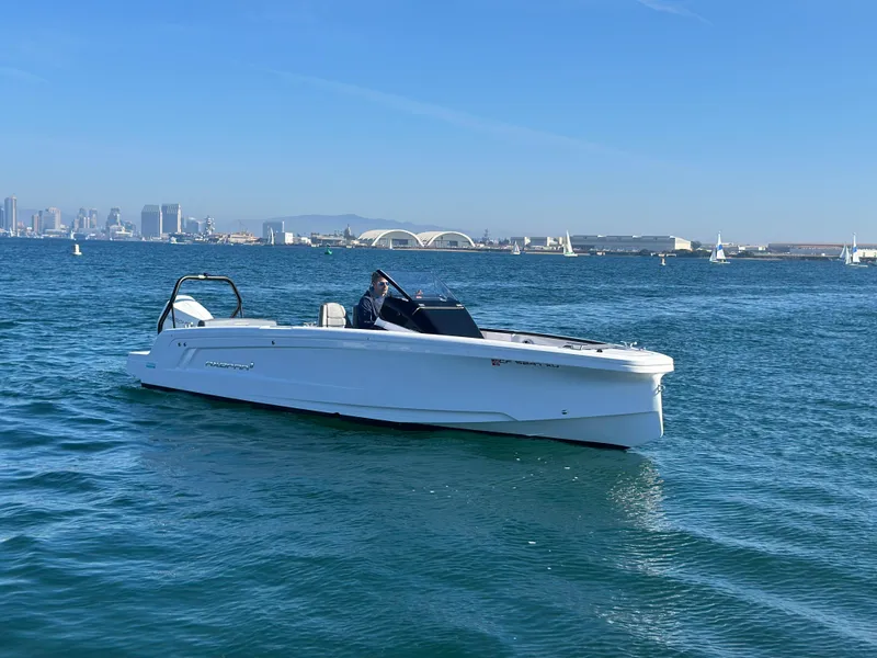 Slide: The Image of 2021 Axopar 22 Spyder boat on calm water with city skyline in background. - 2