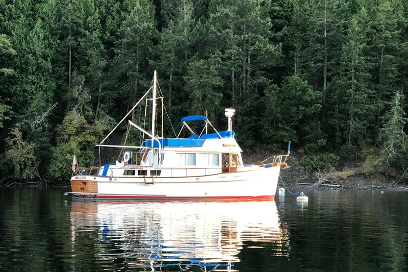 Slide: The Image of 1974 Grand Banks 42 Motoryacht anchored on calm water, surrounded by lush forest. - 50