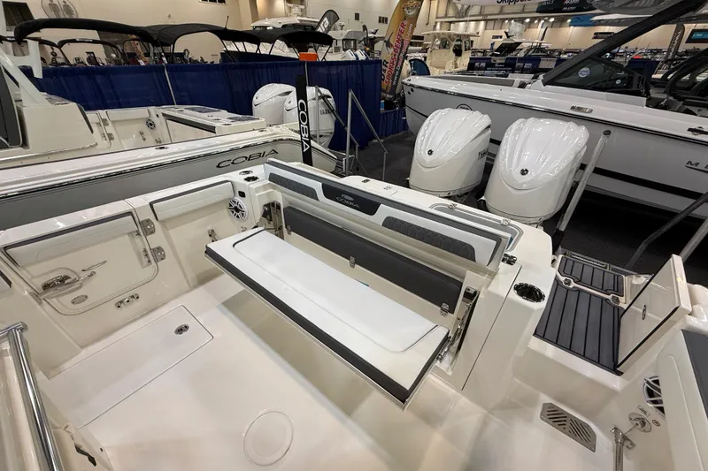 Slide: The Image of 2026 Cobia 285 Center Console boat interior with seating and dual engines at a boat show. - 7
