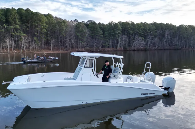 Slide: The Image of 2023 Twin Vee 260 GFX CC boat on a calm lake with forested background. - 23