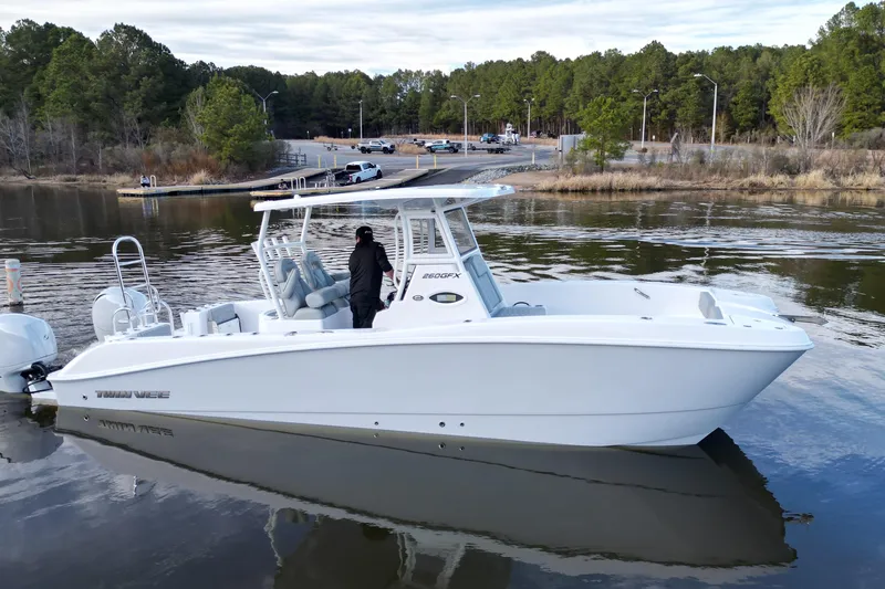 Slide: The Image of 2023 Twin Vee 260 GFX CC boat on calm water near a wooded shoreline. - 28