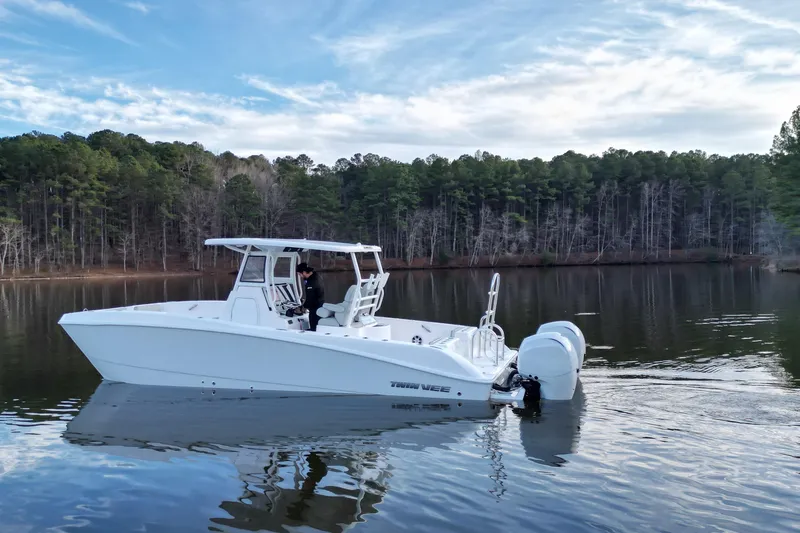 Slide: The Image of 2023 Twin Vee 260 GFX CC boat on a calm lake with forested background. - 32