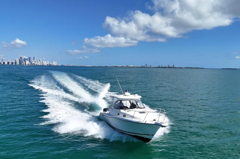 Slide: The Image of 2004 Pursuit 3370 Offshore boat cruising on open water with city skyline in background. - 2