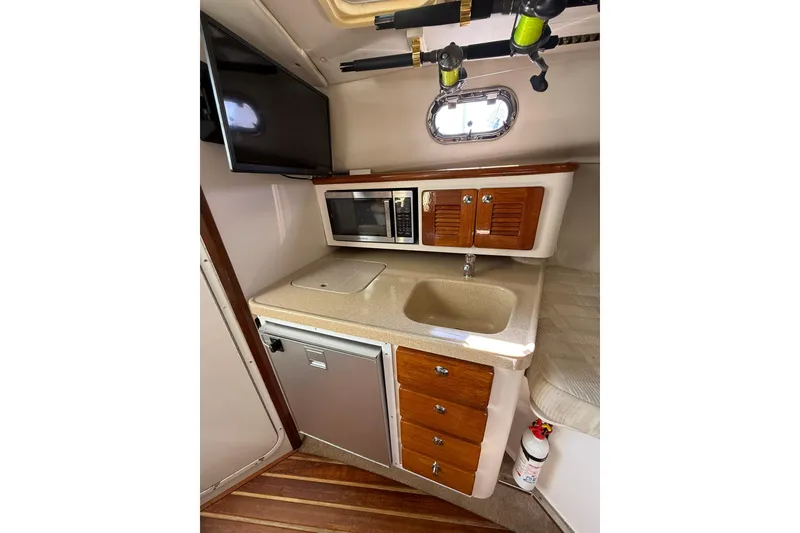 Slide: The Image of 2004 Pursuit 3370 Offshore boat interior with kitchenette, sink, microwave, and TV. - 46