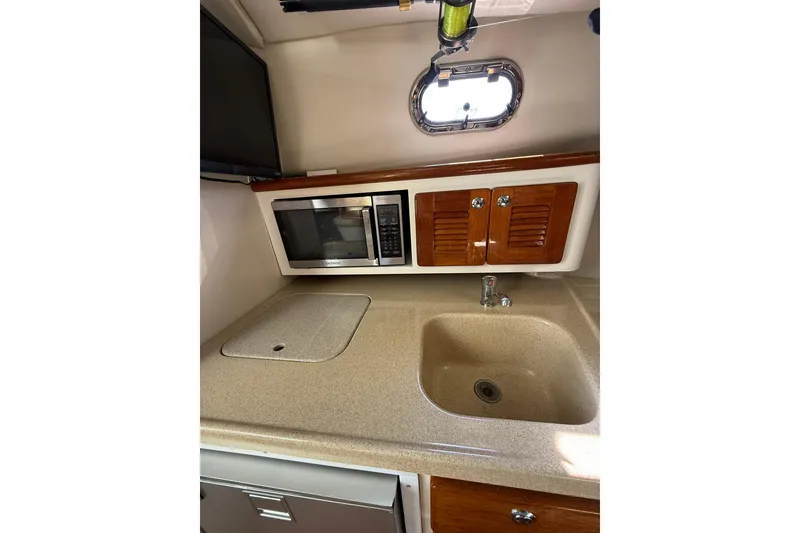Slide: The Image of 2004 Pursuit 3370 Offshore boat kitchen with sink, microwave, and storage cabinets. - 47