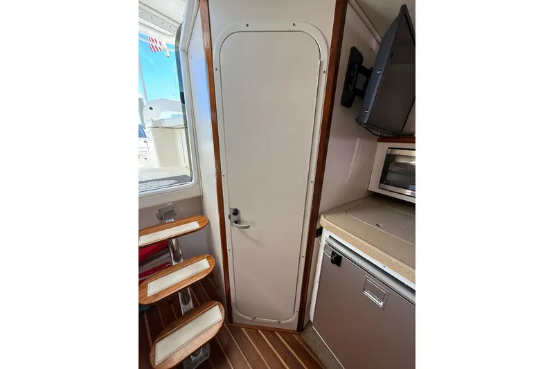 Slide: The Image of 2004 Pursuit 3370 Offshore cabin interior with stairs, door, and kitchenette. - 53