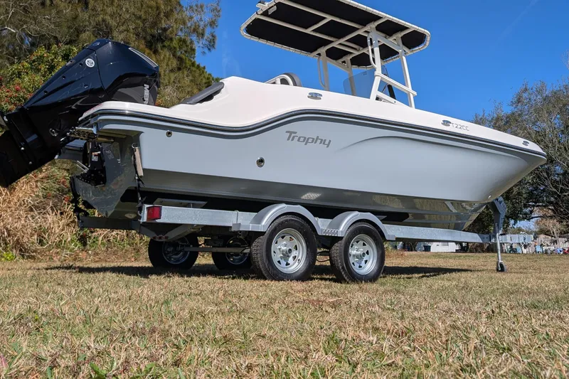 Slide: The Image of 2025 Bayliner Trophy T22CC boat on trailer, parked on grass under clear blue sky. - 7