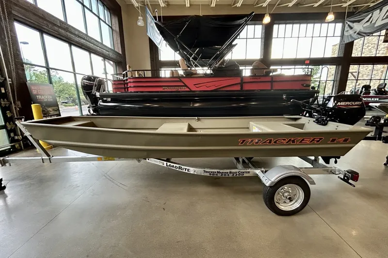 The Image of 2026 Tracker Grizzly 14 Jon boat displayed indoors on a trailer. - 0