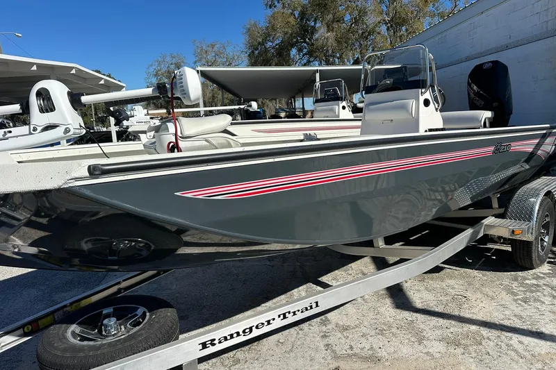Slide: The Image of 2025 Ranger RB210 boat on trailer, gray with red stripes, parked outdoors. - 2