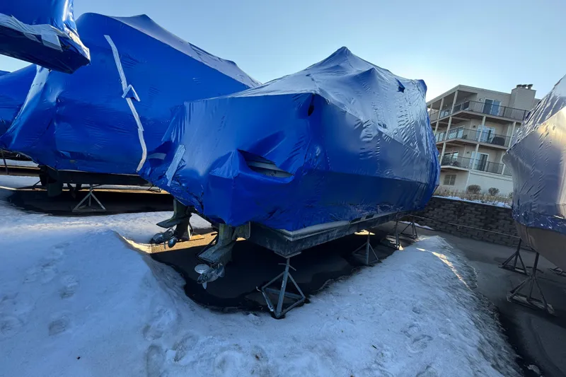 Slide: The Image of 1989 Holiday Mansion Super boat covered in blue tarp, stored on stands in snowy area. - 11