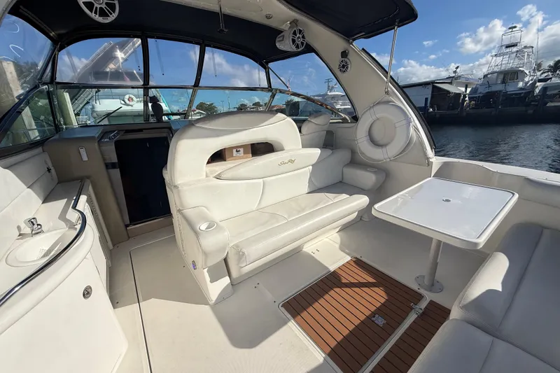 Slide: The Image of 1999 Sea Ray 410 Express Cruiser interior with white seating and table, docked by the water. - 13