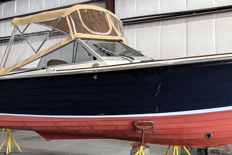 Slide: The Image of 1973 Lyman Islander boat with navy and red hull, tan canopy, stored indoors. - 3