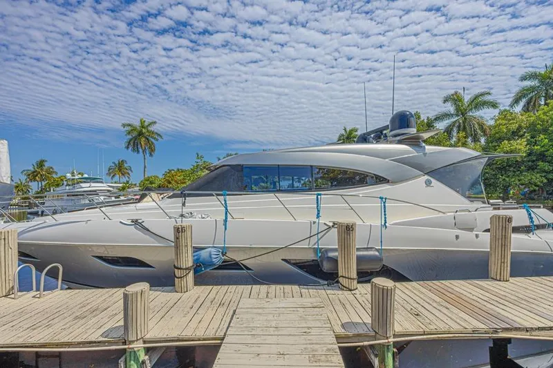 Slide: The Image of 2021 Riviera 6000 Sport Yacht Platinum Edition docked under a partly cloudy sky. - 2