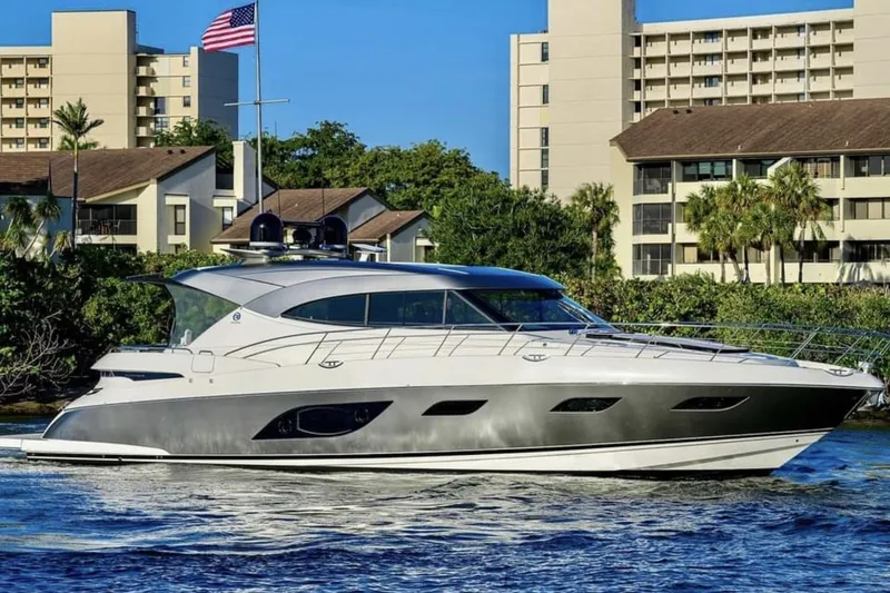 The Image of 2021 Riviera 6000 Sport Yacht Platinum Edition cruising near waterfront buildings. - 0