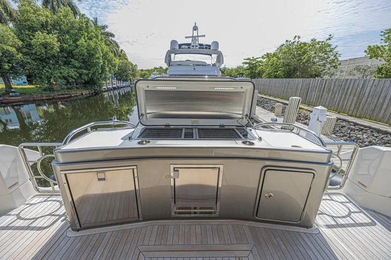Slide: The Image of 2021 Riviera 6000 Sport Yacht Platinum Edition with outdoor kitchen on deck, docked by lush greenery. - 6