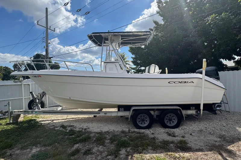 Slide: The Image of 2001 Cobia 254 Center Console boat on trailer, parked outdoors under a sunny sky. - 2