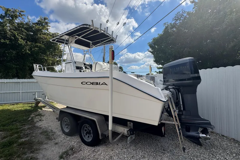 Slide: The Image of 2001 Cobia 254 Center Console boat on trailer, parked outdoors under blue sky. - 4