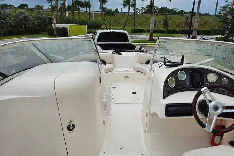 Slide: The Image of 2006 Hurricane SunDeck 237 OB boat interior with steering wheel and seating, parked near palm trees. - 19