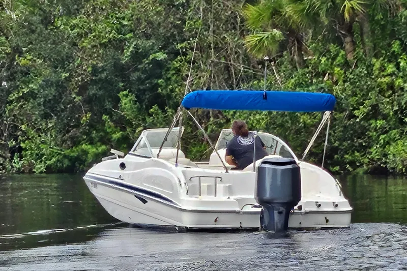 Slide: The Image of 2006 Hurricane SunDeck 237 OB boat cruising on a river with lush greenery. - 24