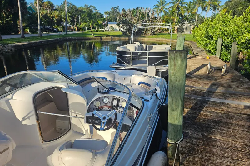 Slide: The Image of 2006 Hurricane SunDeck 237 OB boat docked by a wooden pier, surrounded by lush greenery. - 26