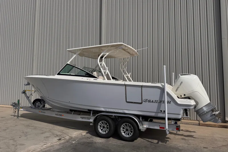 Slide: The Image of 2026 Sailfish 276 DC boat on trailer, parked near a large industrial building. - 2