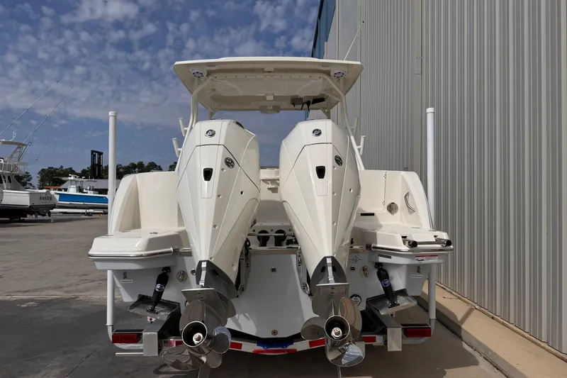 Slide: The Image of 2026 Sailfish 276 DC boat with dual outboard motors, docked near a metal building. - 4