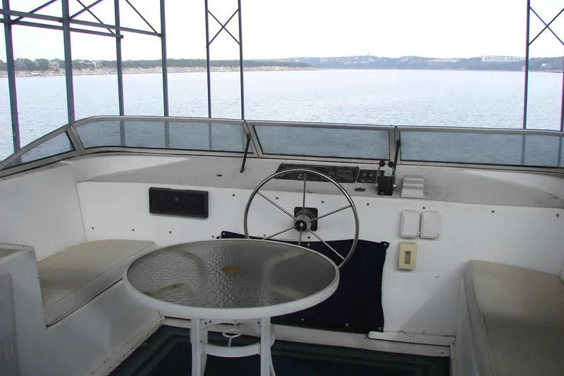 Slide: The Image of 1999 Sumerset 18x90 houseboat helm with glass table, overlooking serene water view. - 4