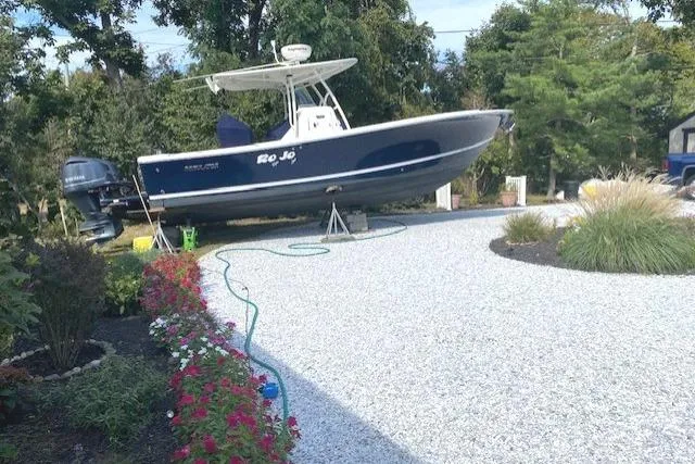 Slide: The Image of 2015 Regulator 28 Forward Seating boat on gravel driveway, surrounded by greenery and flowers. - 7