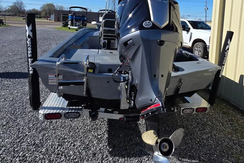 Slide: The Image of 2026 Xpress H24B Bay boat with powerful outboard motor, parked on gravel. - 8