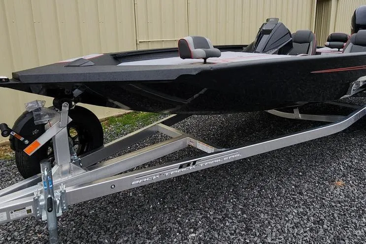 Slide: The Image of 2025 Xpress H20 Bass boat on trailer, parked on gravel near a beige building. - 8