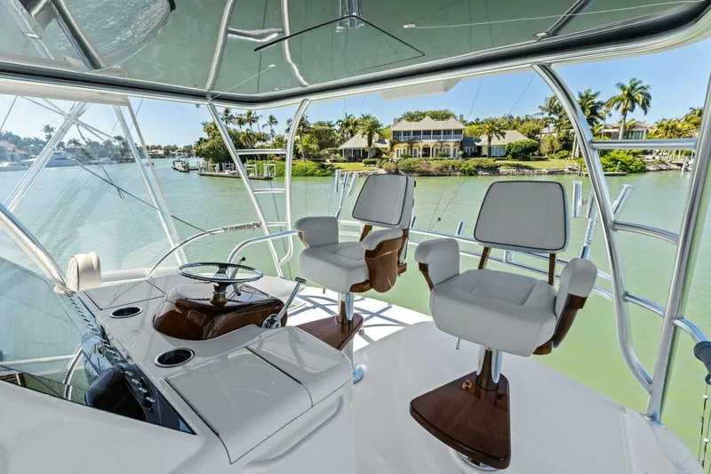 Slide: The Image of 2023 Vikiing convertible yacht interior with helm chairs, overlooking scenic waterfront homes. - 35