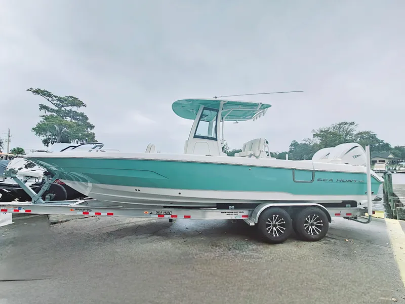 Slide: The Image of 2023 Sea Hunt Escape 28 boat on trailer, parked near waterfront under clear blue sky. - 7