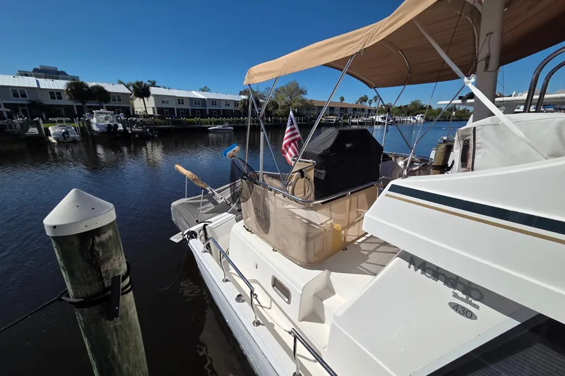 Slide: The Image of 2002 Mainship 430 Trawler docked at marina, featuring tan canopy and American flag. - 16
