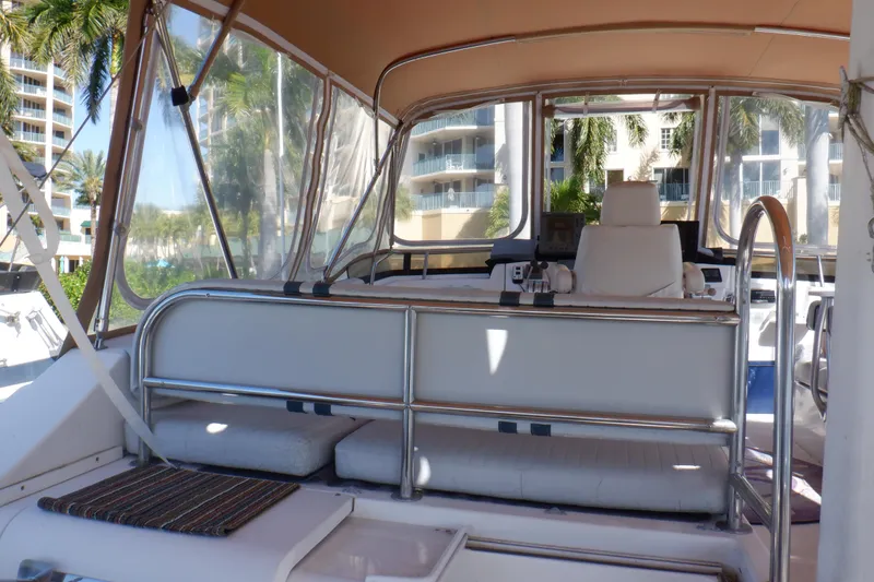 Slide: The Image of 2002 Mainship 430 Trawler helm with seating, surrounded by clear enclosures and tropical backdrop. - 20