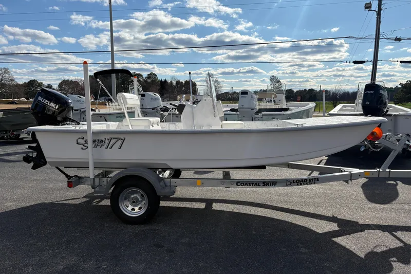 Slide: The Image of 2026 Coastal Skiff 171 boat on trailer, parked outdoors under a partly cloudy sky. - 2