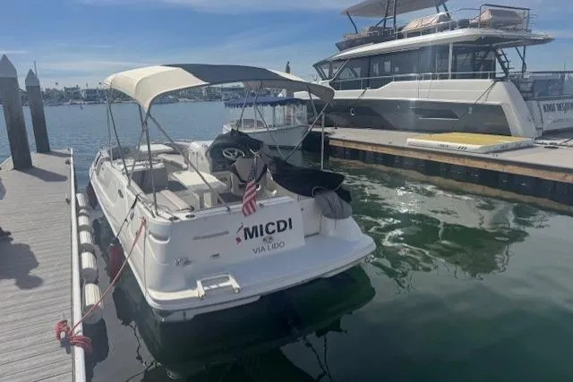 Slide: The Image of 1997 Sea Ray 240 Sundeck docked at marina, featuring canopy and American flag. - 2