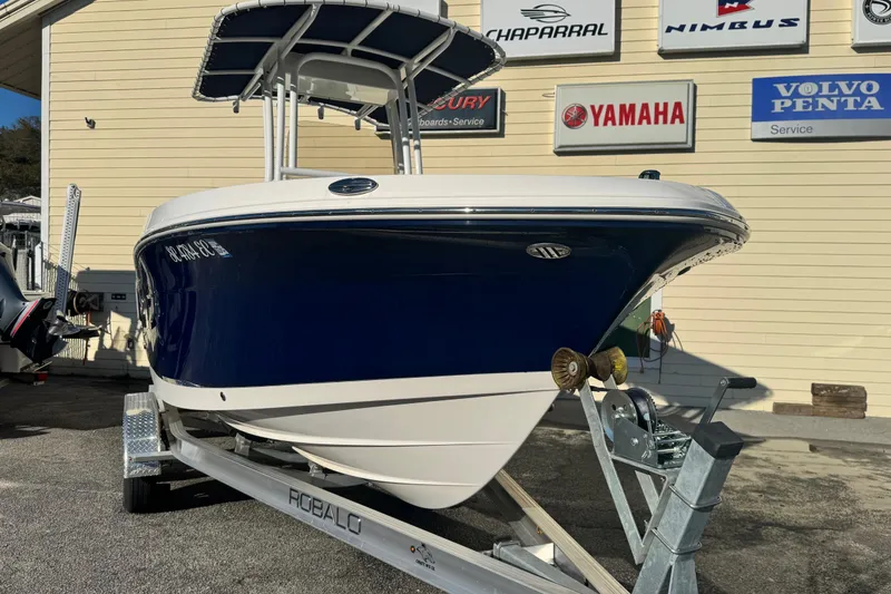 Slide: The Image of 2023 Robalo R202 Explorer boat on trailer, displayed outdoors near dealership signs. - 9