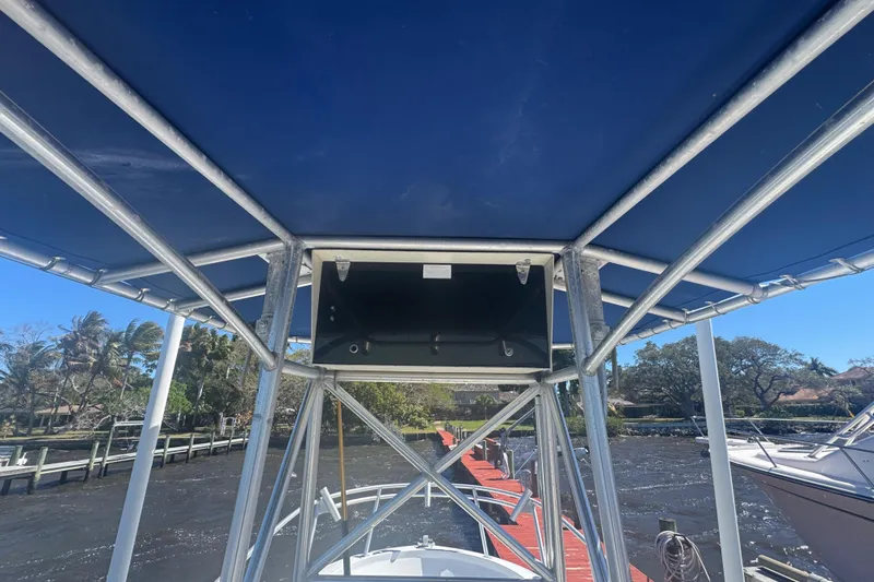Slide: The Image of 1988 Boston Whaler Outrage 17 with blue canopy docked by a scenic waterfront. - 18
