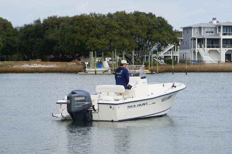 Slide: The Image of 2005 Sea Hunt Triton 202 boat on water, near shoreline with houses and trees. - 2