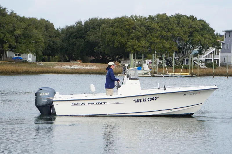 Slide: The Image of 2005 Sea Hunt Triton 202 boat on calm water, with trees and houses in the background. - 3