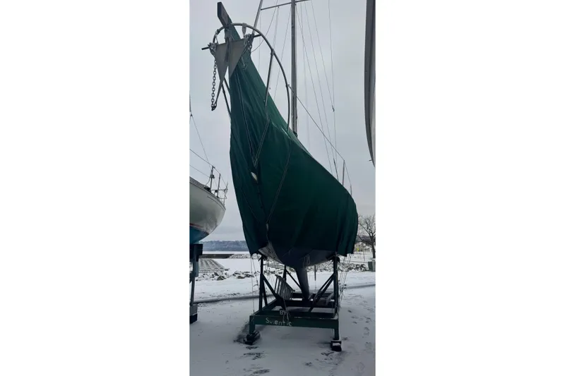 Slide: The Image of 1975 Mirage Yachts 27 sailboat covered in green tarp, stored on snowy ground. - 3