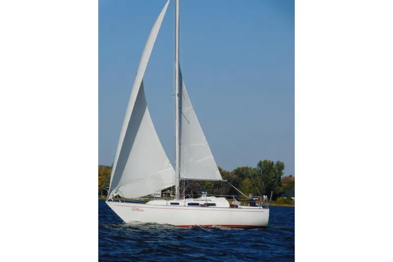 Slide: The Image of 1975 Mirage Yachts 27 sailboat gliding on a serene lake under clear blue skies. - 9